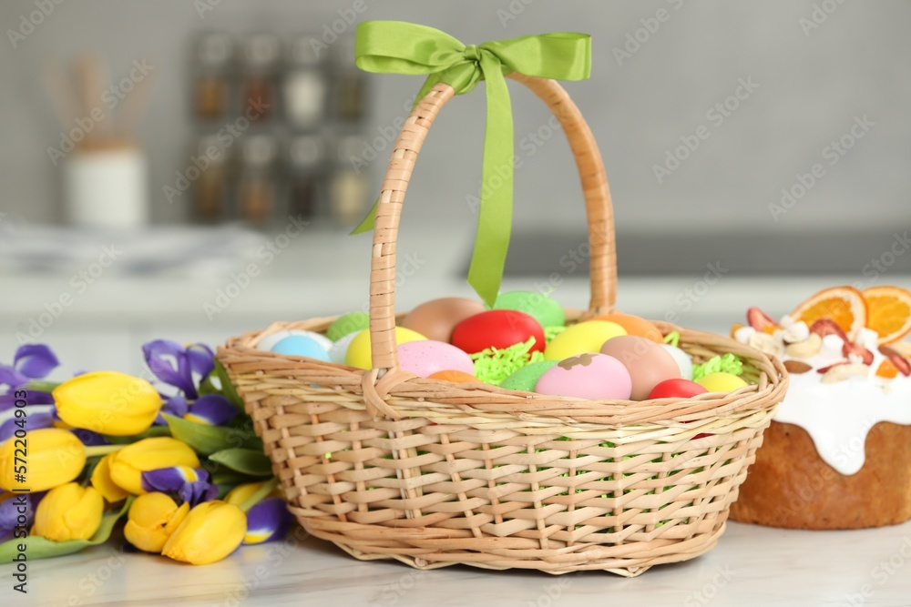 Easter basket with painted eggs between tulips and cake on white marble table indoors Easter basket with painted eggs between tulips and cake on white marble table indoors