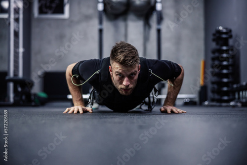 A male fitness instructor in a special department for EMS technology does push-ups and arm exercises in a modern gym concept. Revolution in training  body rehabilitation. Copy space for ads massage