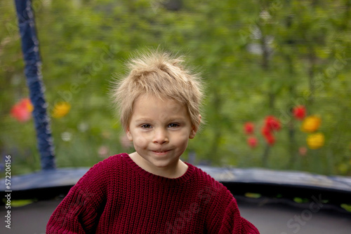 Cute little boy with static electric hair, having his funny portrait taken outdoors on  trampoline