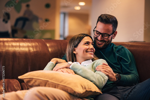 Two colleagues in love relaxing on the couch, looking at each other, smiling.