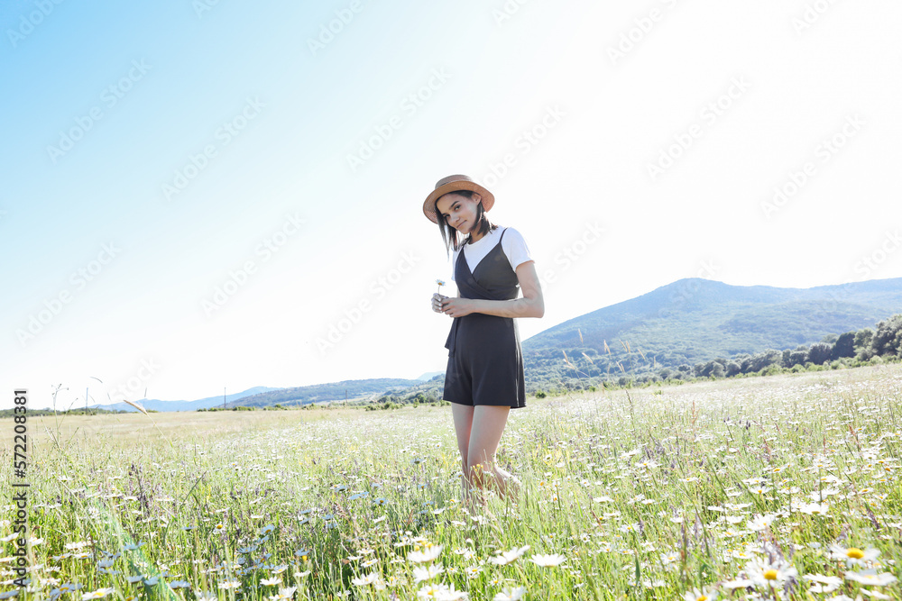 a woman in a hat walks in a field with flowers daisies