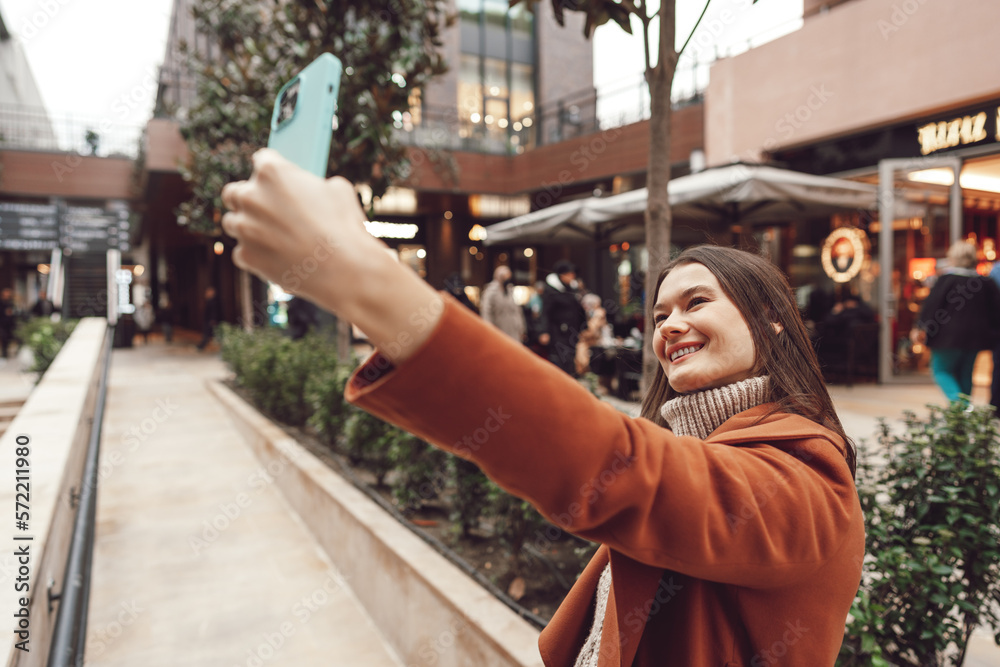 A happy woman in a coat standing on the street and taking a selfie