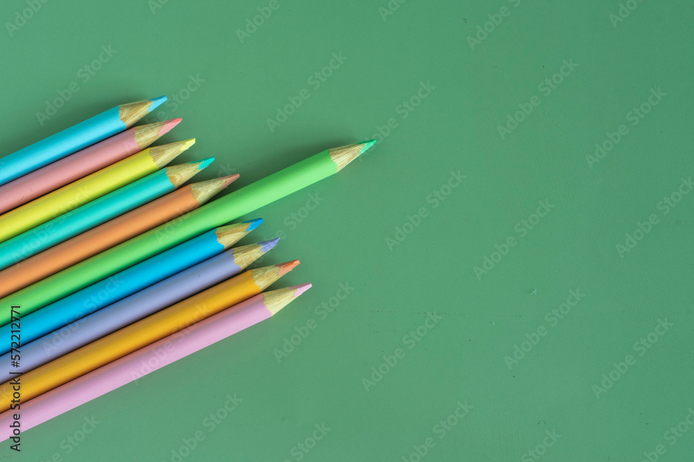 Pastel colored pencils, top view on green background, illustration concept, education and back to school