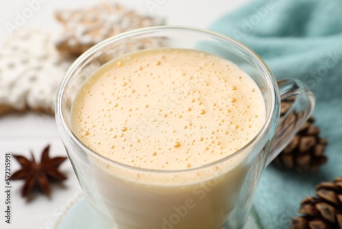 Glass cup with tasty eggnog on white table, closeup