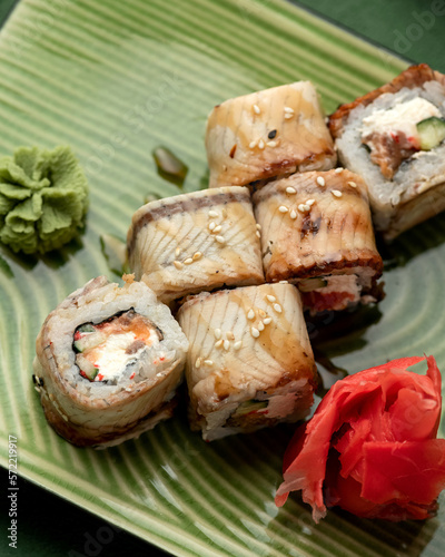 Set of sushi rolls with salmon, eel, cream cheese and cucumber. Rolls on green plate with wasabi and pickled ginger. Seafood dishes. Japanese food. Top view. Close-up. Soft focus.