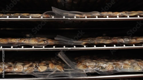 Motion down along metal rack with vacuum packages of delicious fresh fasolari molluscs at seafood processing plant closeup photo