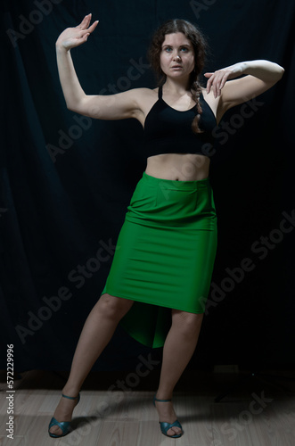 Woman in black top and green skirt posing on black background
