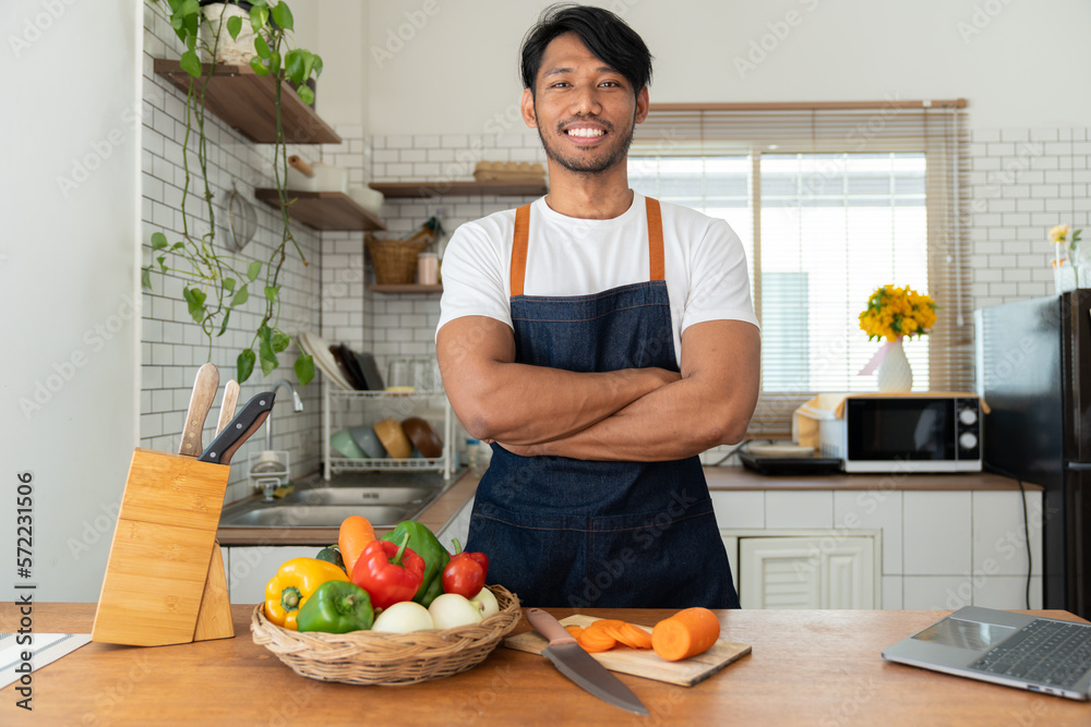 Asian strong man Wearing an apron having fun while preparing ingredients such as fruits and vegetables. learn how to do Chopping Carrots via Application Happily online in the kitchen. Asian strong man Wearing an apron having fun while preparing ingredients such as fruits and vegetables. learn how to do Chopping Carrots via Application Happily online in the kitchen.