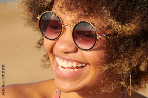 Cheerful girl with braces in fashionable sunglasses. Close-up of laughing girl with dyed frizzy hair with braces wearing stylish round sunglasses on sunny day outdoors.