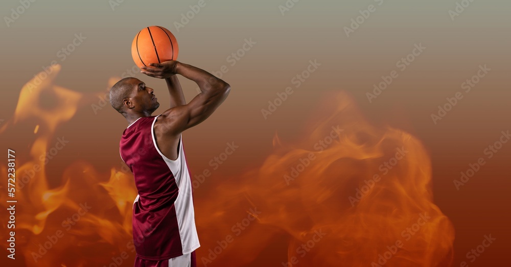 Composition of male basketball player shooting ball, over flames on grey background