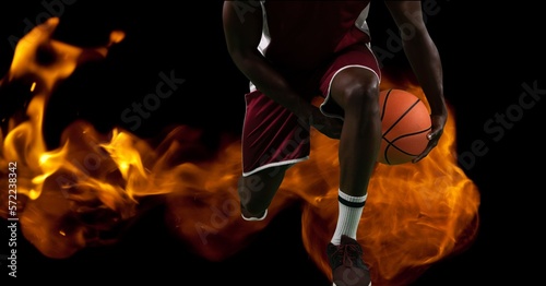 Composition of low section of male basketball player holding ball over flames on black background