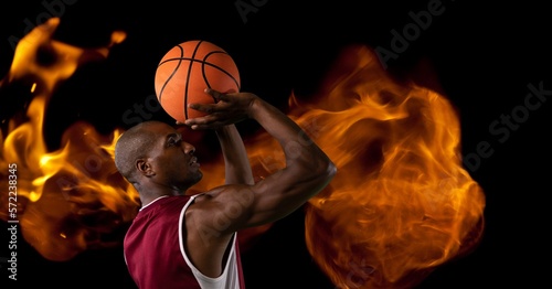 Composition of male basketball player shooting with ball over flames on black background