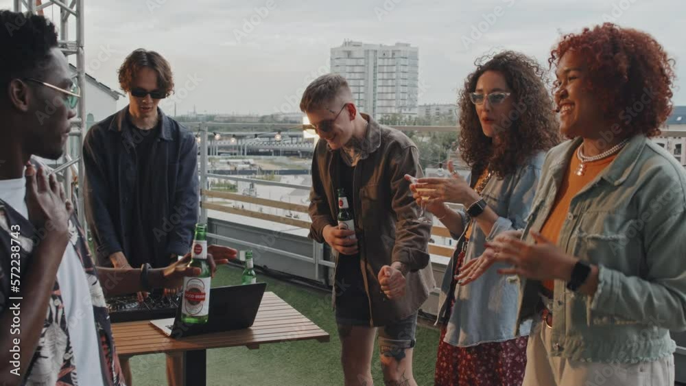 Group of joyful young ethnically diverse men and women wearing stylish casual outfits dancing at party on rooftop on summer evening Group of joyful young ethnically diverse men and women wearing stylish casual outfits dancing at party on rooftop on summer evening