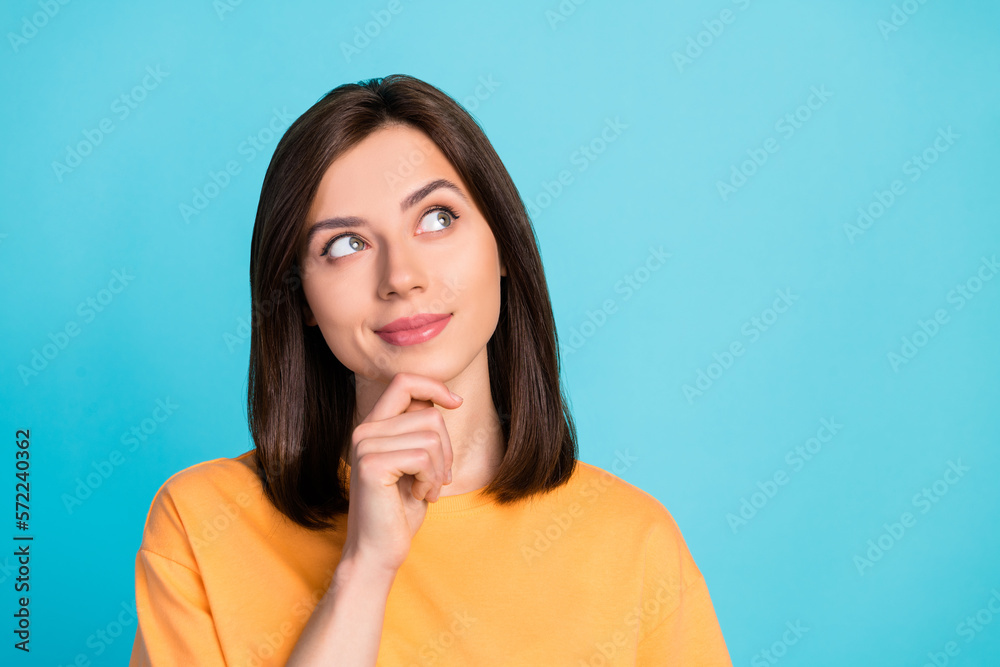 Portrait of thoughtful minded girl with long hairdo dressed yellow t-shirt look empty space hand on chin isolated on blue color background Portrait of thoughtful minded girl with long hairdo dressed yellow t-shirt look empty space hand on chin isolated on blue color background