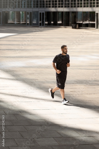 Handsome strong sportsman running at the street outdoors and looking aside 