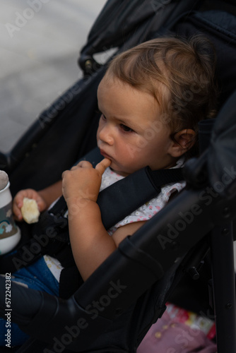 Kleinkind im Kinderwagen nachdenklich und skeptisch mit etwas zu essen in der rechten Hand photo