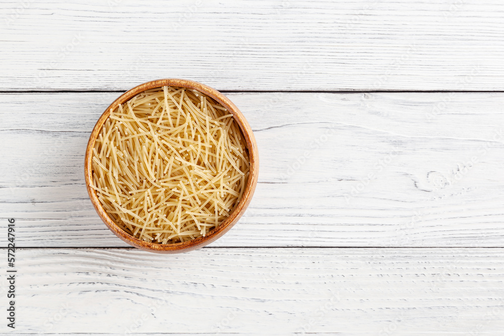 Uncooked filini pasta in wooden bowl on white wooden background with copy space