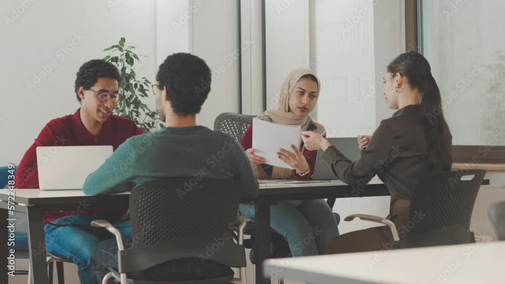 Young multiethnic business team sitting at table in modern office discussing business documents and brainstorming ideas