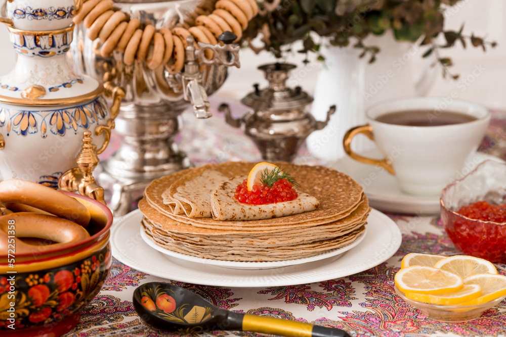 Russian traditions. Russian holiday Maslenitsa. Still life with a cup of tea, a stack of pancakes, red caviar, lemon, bagels, a lollipop cockerel, wooden spoons (khokhloma) and samovars. Russian traditions. Russian holiday Maslenitsa. Still life with a cup of tea, a stack of pancakes, red caviar, lemon, bagels, a lollipop cockerel, wooden spoons (khokhloma) and samovars.