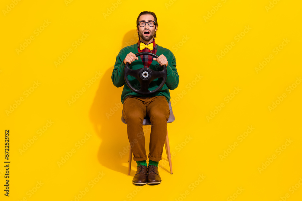 Full body photo of impressed scared guy open mouth sit chair arms hold wheel isolated on yellow color background Full body photo of impressed scared guy open mouth sit chair arms hold wheel isolated on yellow color background