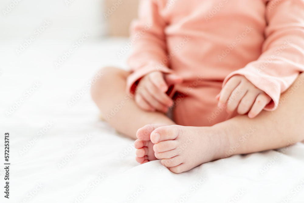 close-up of the legs and arms of a small baby on a light white bed close-up of the legs and arms of a small baby on a light white bed
