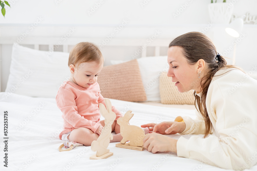 mom plays with her little daughter with wooden toys at home on the bed and have fun together, family and motherhood