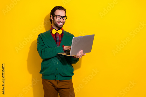 Photo portrait of young handsome man eyewear holding laptop toothy smile wear trendy green garment isolated on yellow color background