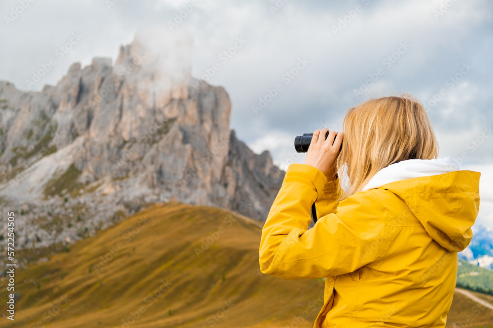 Young blonde woman looks in binoculars to high mountain pass in the Dolomites, the Giau Pass. Young blonde woman looks in binoculars to high mountain pass in the Dolomites, the Giau Pass.
