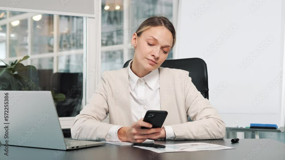 Closeup happy businesswoman using mobile phone tapping message at workplace. Smiling woman browsing internet on smartphone in office. Portrait of business woman reading messages on cellphone.