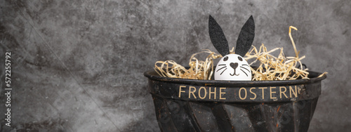 Frohe Ostern Feiertag Hintergrund Grußkarte mit Text  - Süßer Osterhase Osterei in Osternest aus alter Kuchenform mit Beton Wand photo