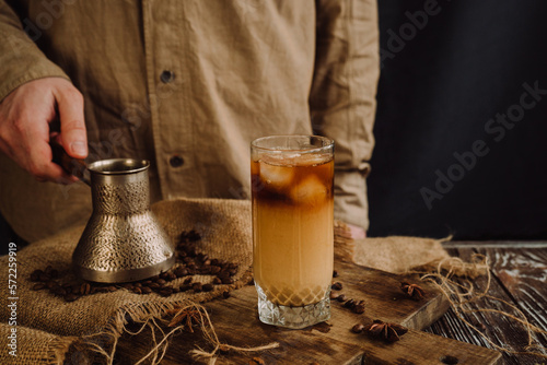  a glass of refreshing cold coffee with ice and milk is standing on a wooden table near a male barista 2