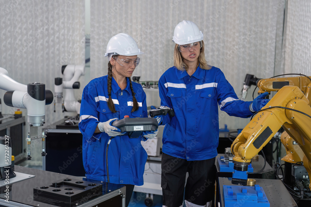 Female senior robotic engineer in modern factory teach new comer operate and maintenance robot arm Female senior robotic engineer in modern factory teach new comer operate and maintenance robot arm