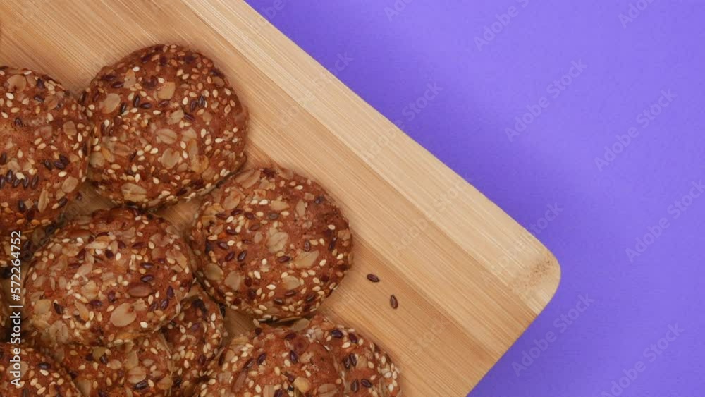 Rotation Of Oatmeal Cookies With Sesame Seeds On A Wooden Board On A Purple Background On The Left Side. Top View. 4k, ProRes