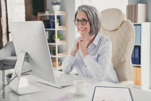 Photo of positive smiling lady boss wear white shirt eyeglasses reading twitter telegram facebook messages indoors workplace workstation