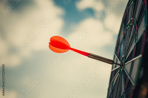 Close up shot of the dart arrow hit on bulleyes of dartboard to represent that the business reached the target with dark tone picture style. Target and goal as concept.