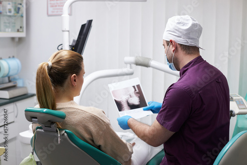 Caring male dentist doctor, showing the x-ray image to the patient sitting on dentist's seat.