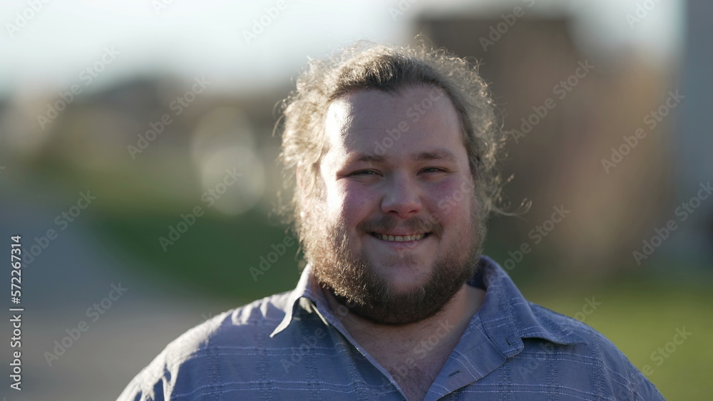 One happy overweight young man smiling at camera standing outdoors in sunlight. Natural casual male caucasian person looking at camera One happy overweight young man smiling at camera standing outdoors in sunlight. Natural casual male caucasian person looking at camera