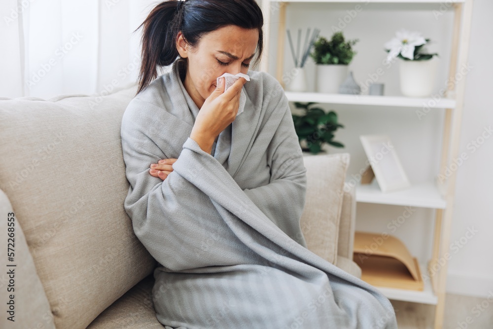 Woman cold headache runny nose and stuffy nose sitting on sofa in plaid, treatment for flu, allergies and covid-19 Woman cold headache runny nose and stuffy nose sitting on sofa in plaid, treatment for flu, allergies and covid-19