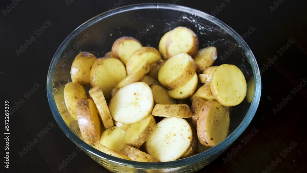 Potatoes marinated in baking spices are in a glass bowl. Potatoes marinated in baking spices are in a glass bowl.
