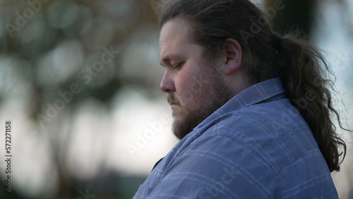 Close up young man typing on laptop sitting outside at park. One chubby casual male caucasian person working remotely in front of computer screen outdoors
