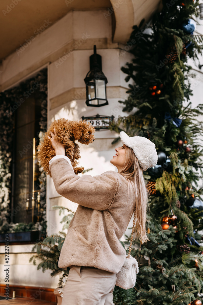 Young woman holding a puppy, smiling, standing on christmas city background