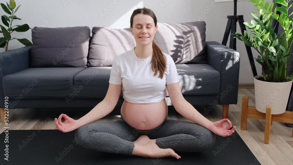 Peace of mind. Beautiful happy young pregnant woman do prenatal yoga exercises meditate in lotus pose at home feel relaxed stress free. Smiling calm future mother to be control emotions in meditation Peace of mind. Beautiful happy young pregnant woman do prenatal yoga exercises meditate in lotus pose at home feel relaxed stress free. Smiling calm future mother to be control emotions in meditation