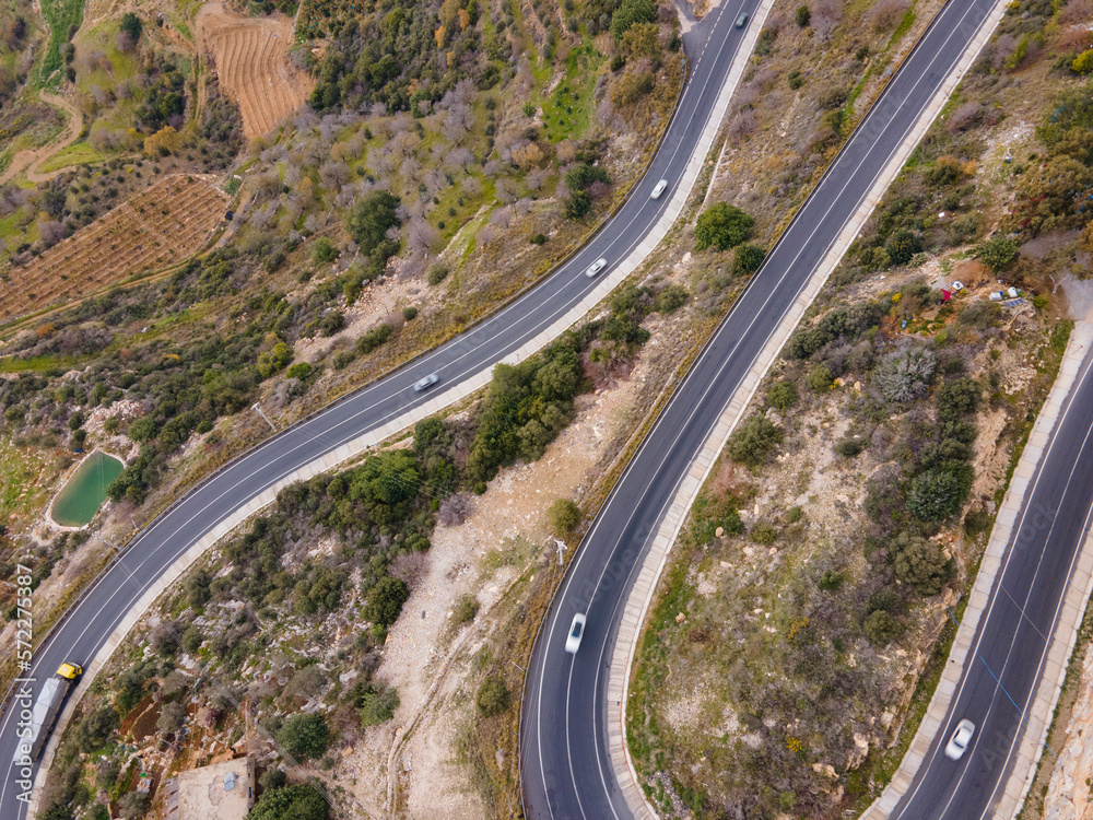 aerial shot of cars passing through a spiral road surrounded by trees in the countryside