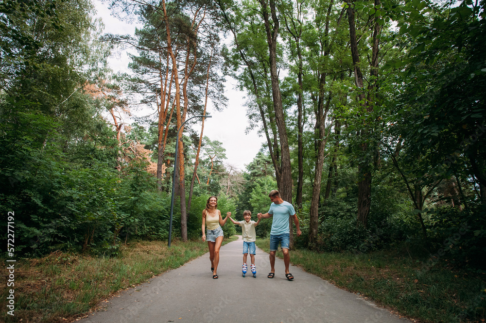 A happy young family, dad, mom and son are skating hand in hand with their parents, on roller skates, along a path in the park. The whole family is dressed in shorts and T-shirts. A happy young family, dad, mom and son are skating hand in hand with their parents, on roller skates, along a path in the park. The whole family is dressed in shorts and T-shirts.