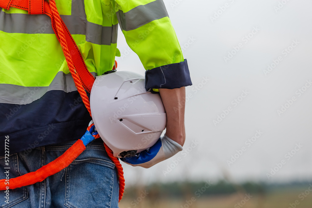 man engineer holding helmet safety wearing uniform standing  at wind turbine field renewable energy. technology protect environment reduce global warming problems. back view.