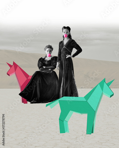 Creative portrait of two beautiful women in image of queen and princess with bubble gum and 3d origami model of horses over light background. Surrealism