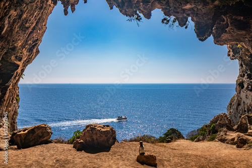 Gagliano del Capo. The spectacular Cipolliane caves, on the rocky cliff of Salento. A little girl admires the amazing panorama of the blue sea and a speedboat goes by. The entrance to the cave.