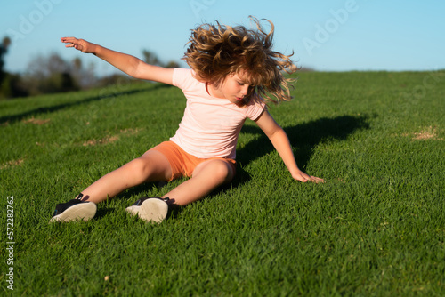 Child running tripped and falls down. Kid runs through the spring grass and falling down on the ground in park. Fall risk for children. Injured, safety, dangerous and incident concept.