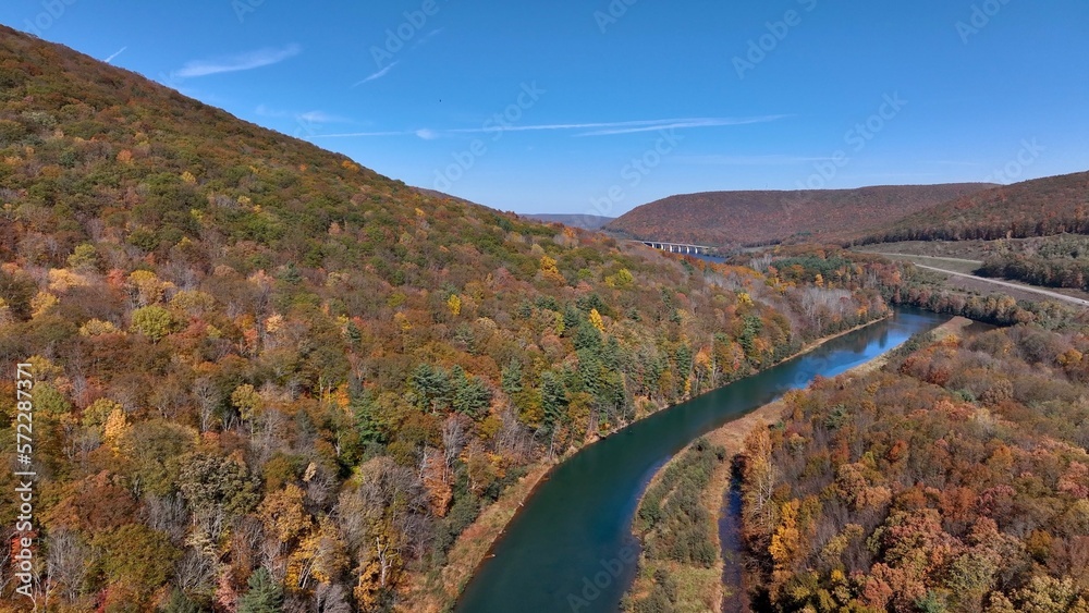 River beside mountains during Autumn with Fall colors under blue sky in American nature area wilderness forest