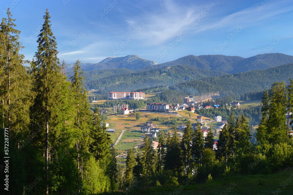 Summer morning in Carpathian mountains. View on the Bukovel ski resort. Coniferous trees in the foreground.